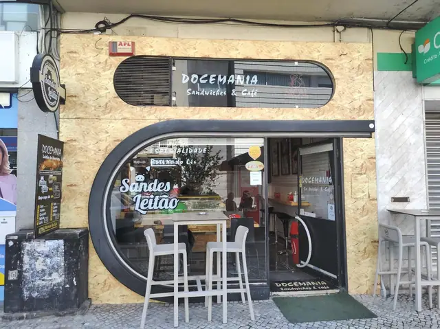 Fachada da Docemania na Avenida Heróis de Angola, revestida a madeira, com montra oval e mesas altas na calçada