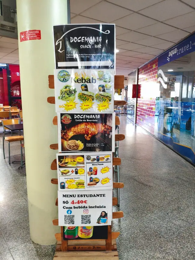Expositor de madeira com cartazes da Docemania: leitão da Boa Vista, kebab, bifana e menu estudante