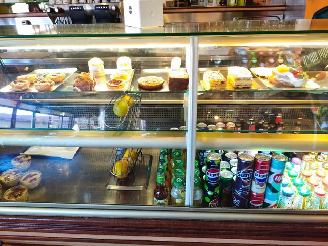 Vitrine refrigerada com pastéis de nata, queijadas, mil-folhas e bolos, e bebidas na prateleira de baixo