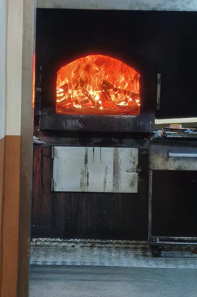 Forno a lenha aceso, com as chamas visíveis pela porta