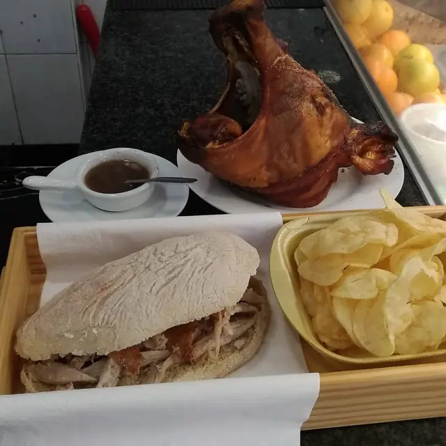 Sandes de leitão com batatas fritas e uma taça de molho, com uma cabeça de leitão assada ao fundo